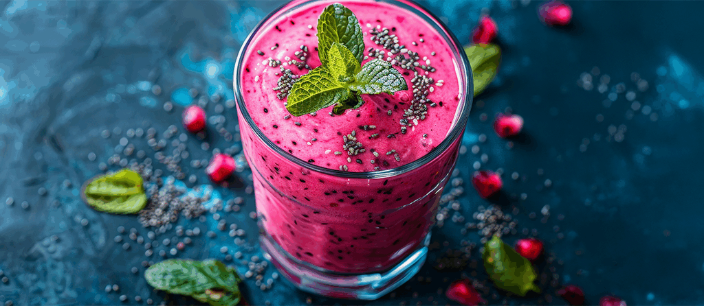 Heldere roze dieet shakes in een glas voor snel afvallen. Het glas is gegarneerd met verse muntblaadjes en chiazaad, op een blauw marmeren oppervlak met verspreide muntblaadjes en rode bessen.